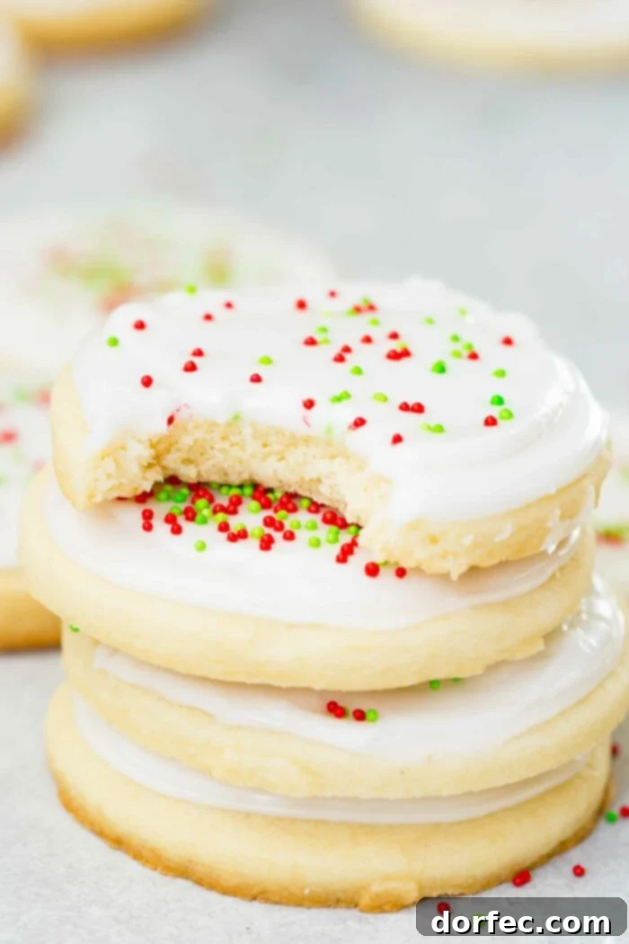 Stack of four festive white chocolate sugar cookies with peppermint royal icing, adorned with red and green sprinkles, with a bite taken from the top cookie. Perfect for Christmas baking.
