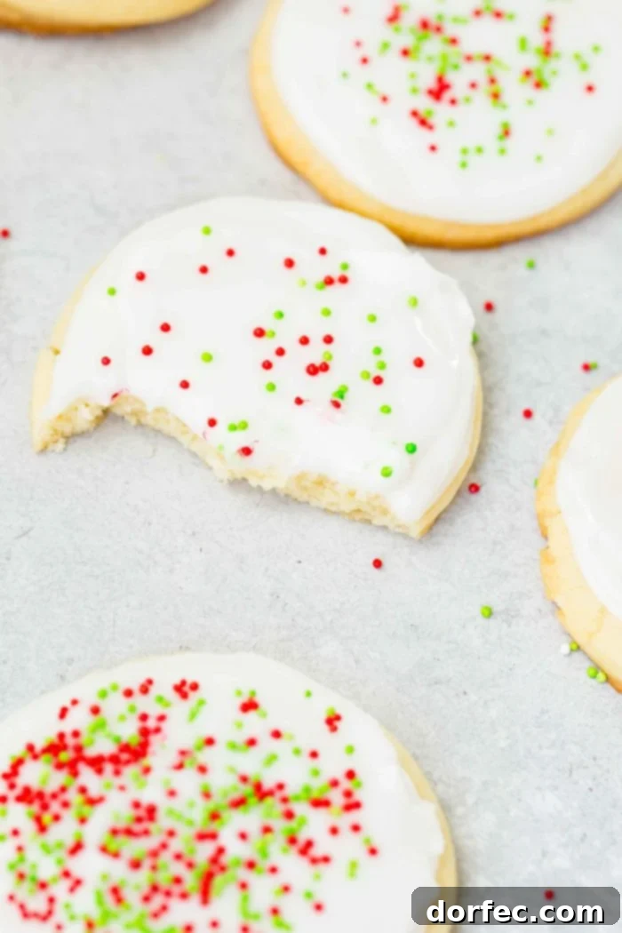 Close-up of several white chocolate sugar cookies with peppermint royal icing and festive red and green sprinkles, one with a missing bite, showcasing their soft texture and beautiful decoration.