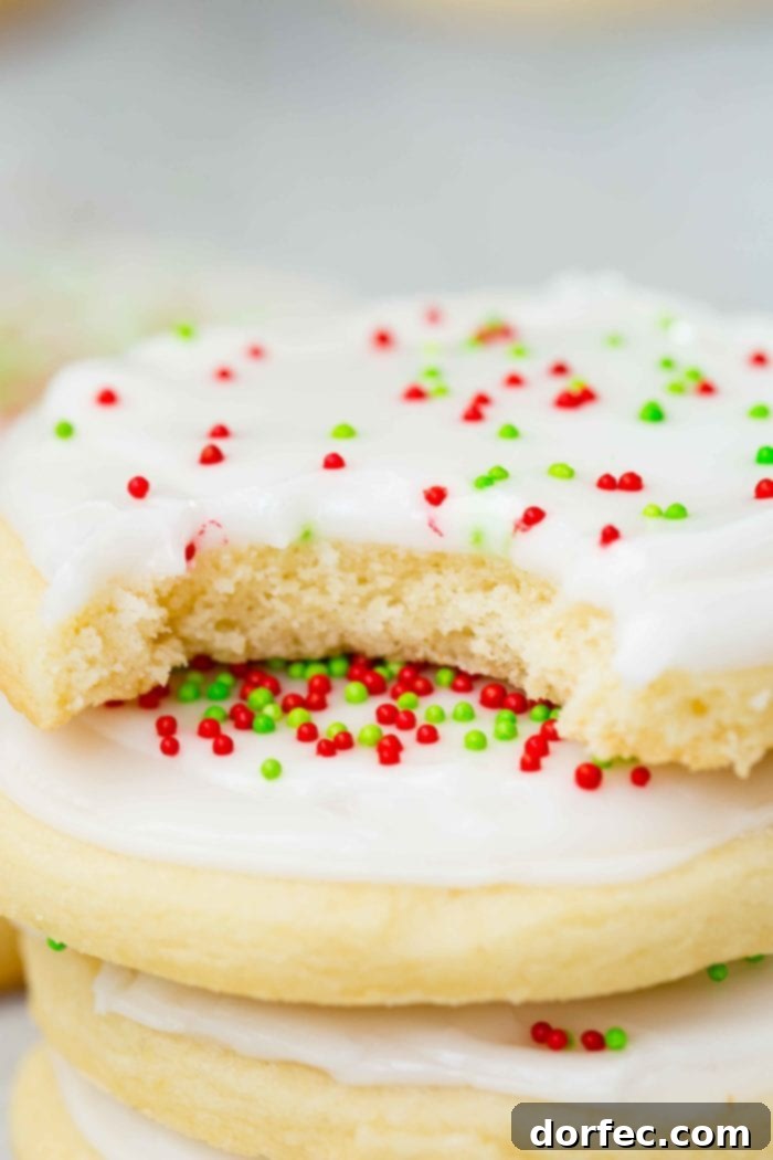 A tantalizing close-up of a stack of four white chocolate sugar cookies, topped with peppermint royal icing and festive red and green sprinkles, with a bite taken from the top cookie, highlighting its soft texture.