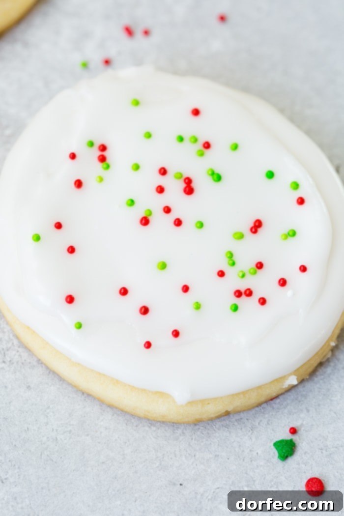 A close-up shot of a single white chocolate sugar cookie, beautifully frosted with smooth peppermint royal icing and adorned with festive red and green sprinkles, highlighting the delicate details.