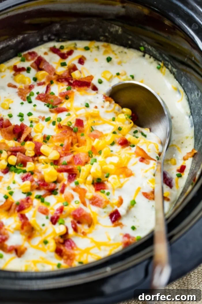 A bowl of creamy slow cooker potato broccoli corn chowder with bacon, garnished with chives and a silver ladle on the side.