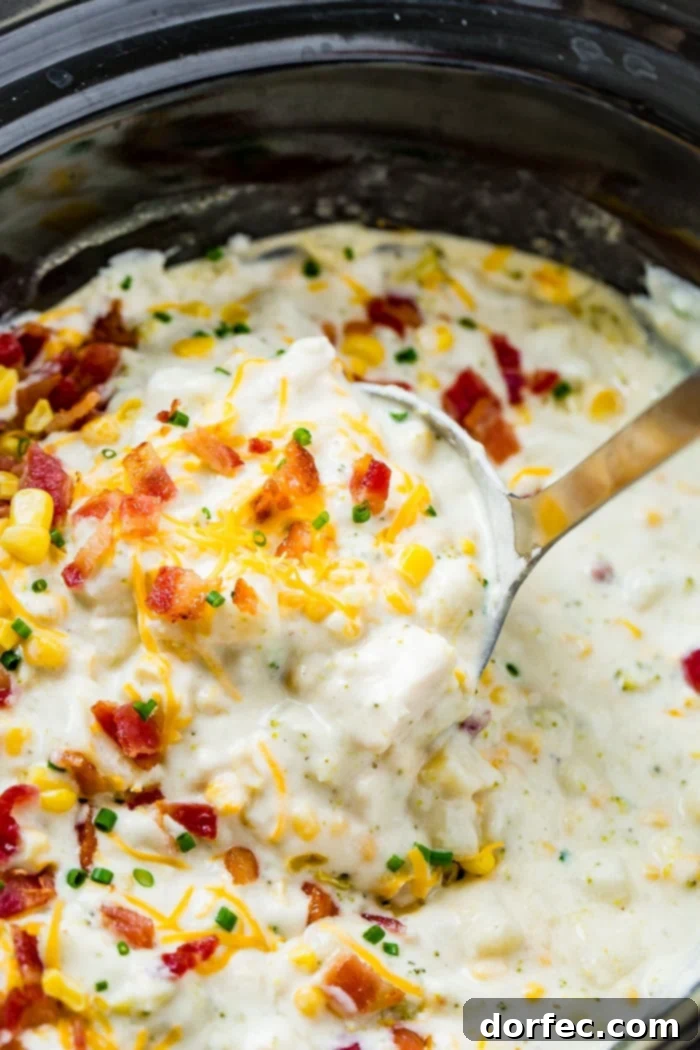 A white bowl full of steaming slow cooker potato broccoli corn chowder with bacon, garnished with chives on a dark background.