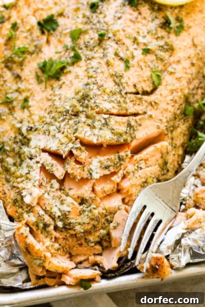 A close-up of a baked salmon fillet flaked with a fork, showing its tender and juicy texture, garnished with fresh parsley