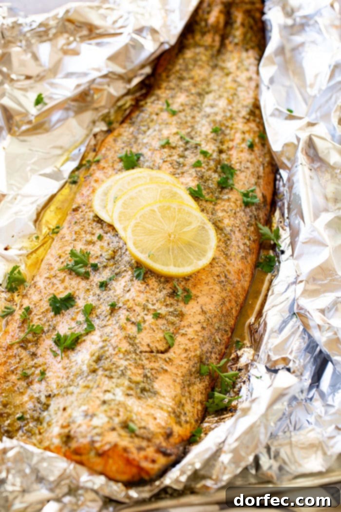 A baked salmon fillet in aluminum foil, garnished with fresh parsley and lemon slices, showcasing its elegant presentation