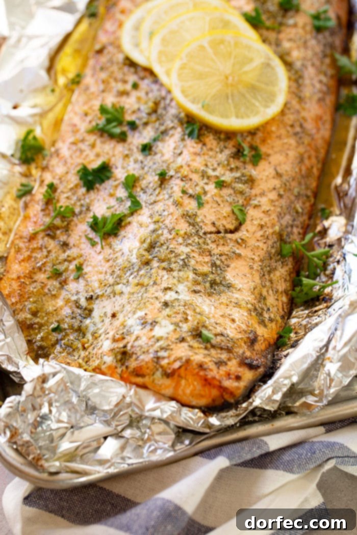 A baked salmon fillet in aluminum foil, garnished with fresh parsley and lemon slices, ready for serving
