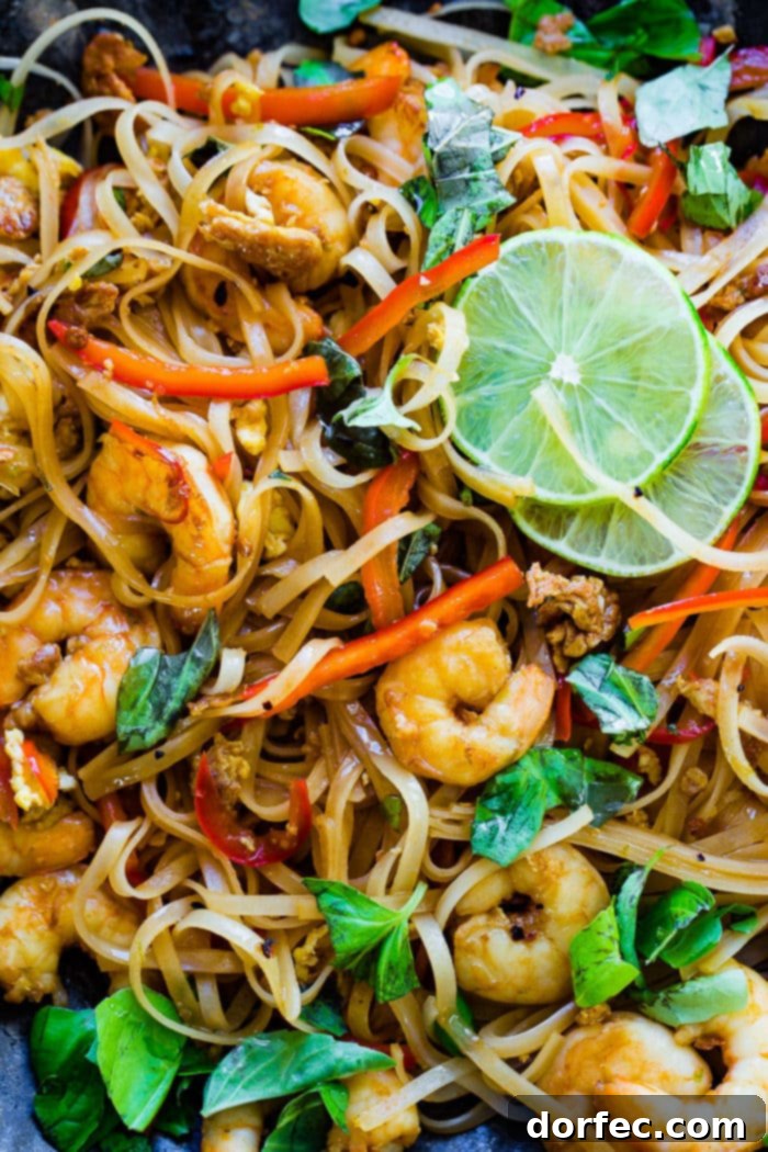 A closeup photo of cooked shrimp, rice noodles, red bell peppers, and fresh basil leaves on a blue plate garnished with slices of lime.