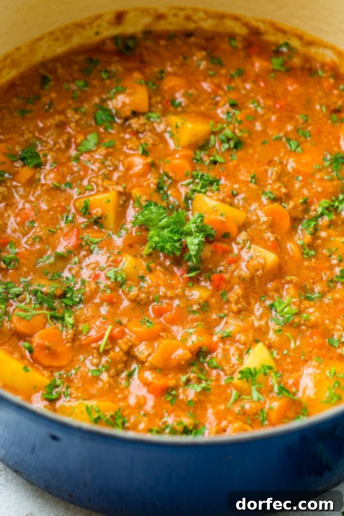 A vibrant blue Le Creuset pot filled with steaming quick and easy ground beef stew, showcasing tender potatoes, carrots, and a sprinkle of fresh parsley on top.