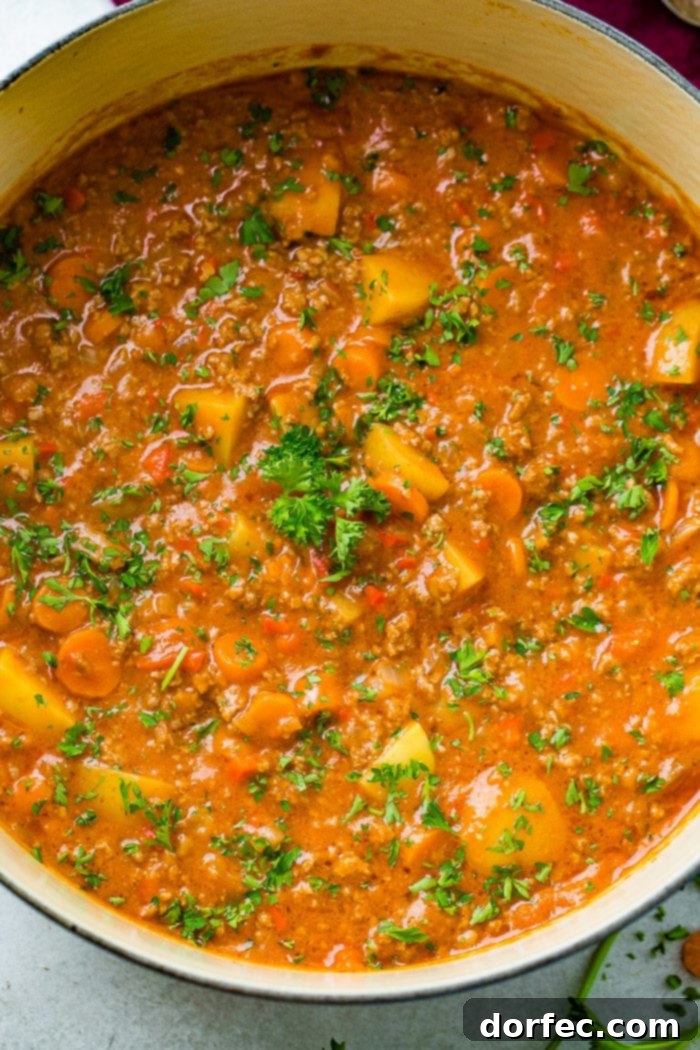 A blue Le Creuset pot filled with steaming quick and easy ground beef stew, showcasing tender potatoes, carrots, and a sprinkle of fresh parsley on top.