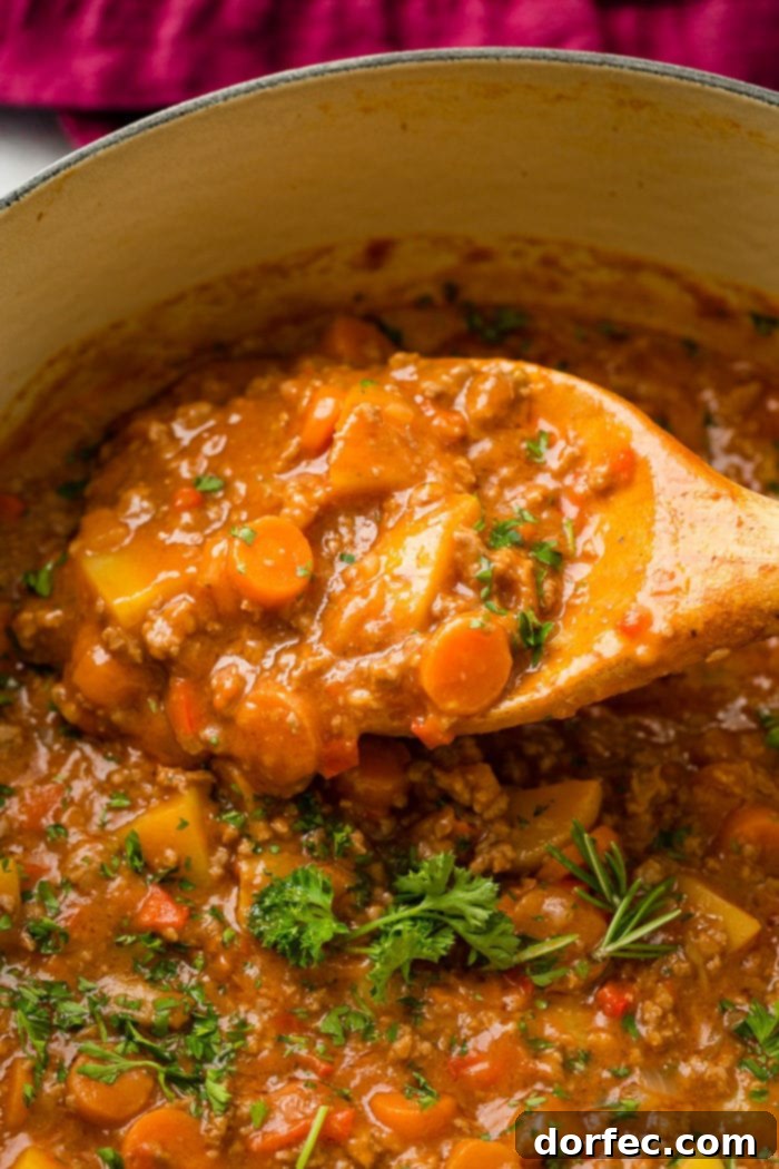 A blue Le Creuset pot filled with steaming quick and easy ground beef stew, showcasing tender potatoes, carrots, and a sprinkle of fresh parsley on top.