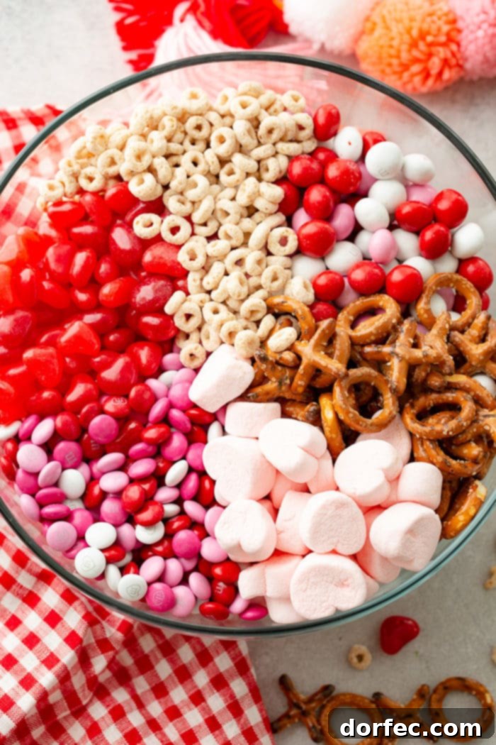A vibrant glass bowl brimming with a festive Valentine's Snack Mix, featuring frosted Cheerios, colorful Valentine's M&M's, sweet and salty X and O shaped pretzels, fluffy pink heart marshmallows, and chewy Starburst jelly beans.