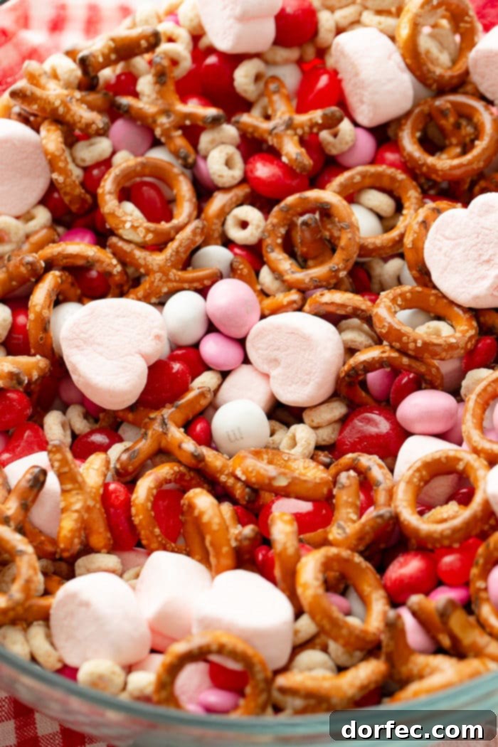 A vibrant and appetizing close-up of the Valentine's Snack Mix, highlighting the variety of textures and festive colors from the Cheerios, M&M's, pretzels, marshmallows, and Starburst jelly beans.