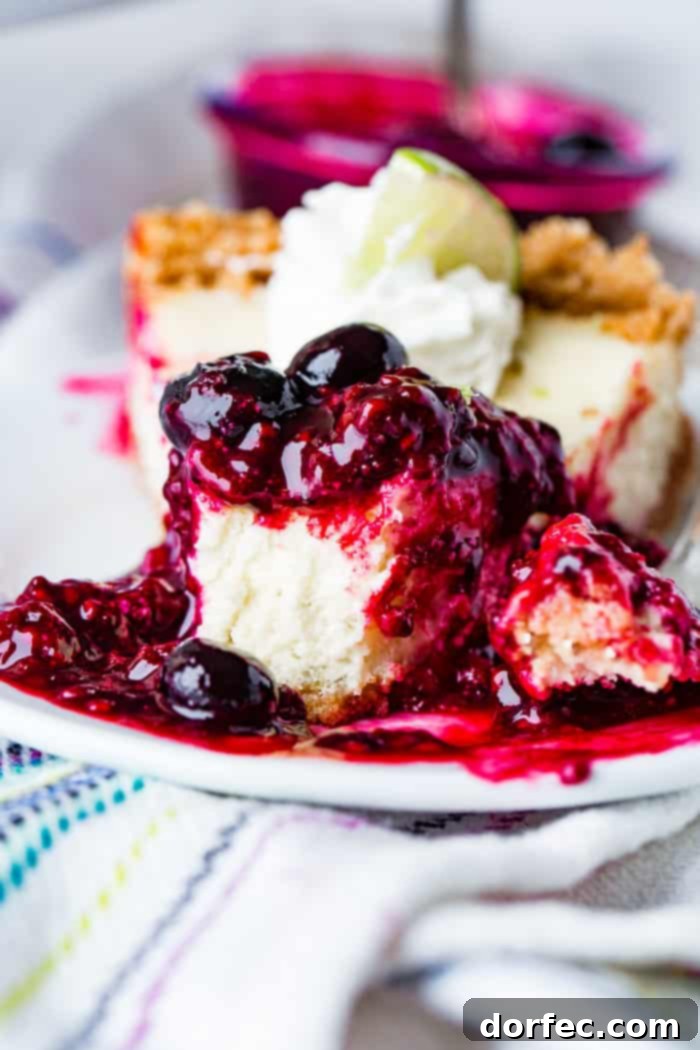 A close-up, enticing photo of a slice of lime cheesecake on a white plate, with a bite playfully taken out. The luscious triple berry sauce cascades around the slice, inviting a decadent taste experience.