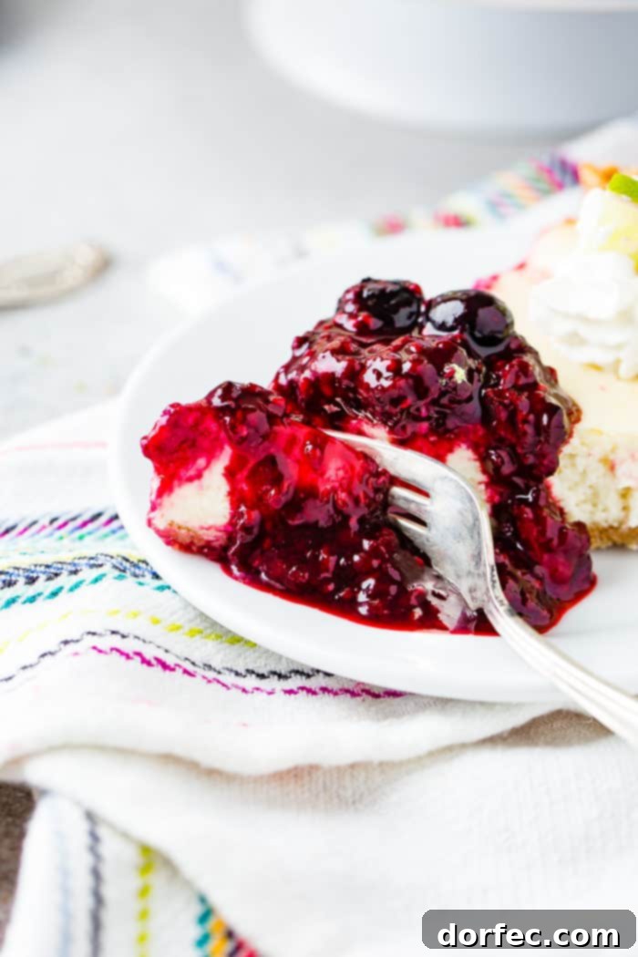 A tantalizing photo of a slice of lime cheesecake, lavishly adorned with triple berry sauce, being gently cut into with a fork on a crisp white plate. The berry sauce artfully drips around the slice, promising a burst of flavor.