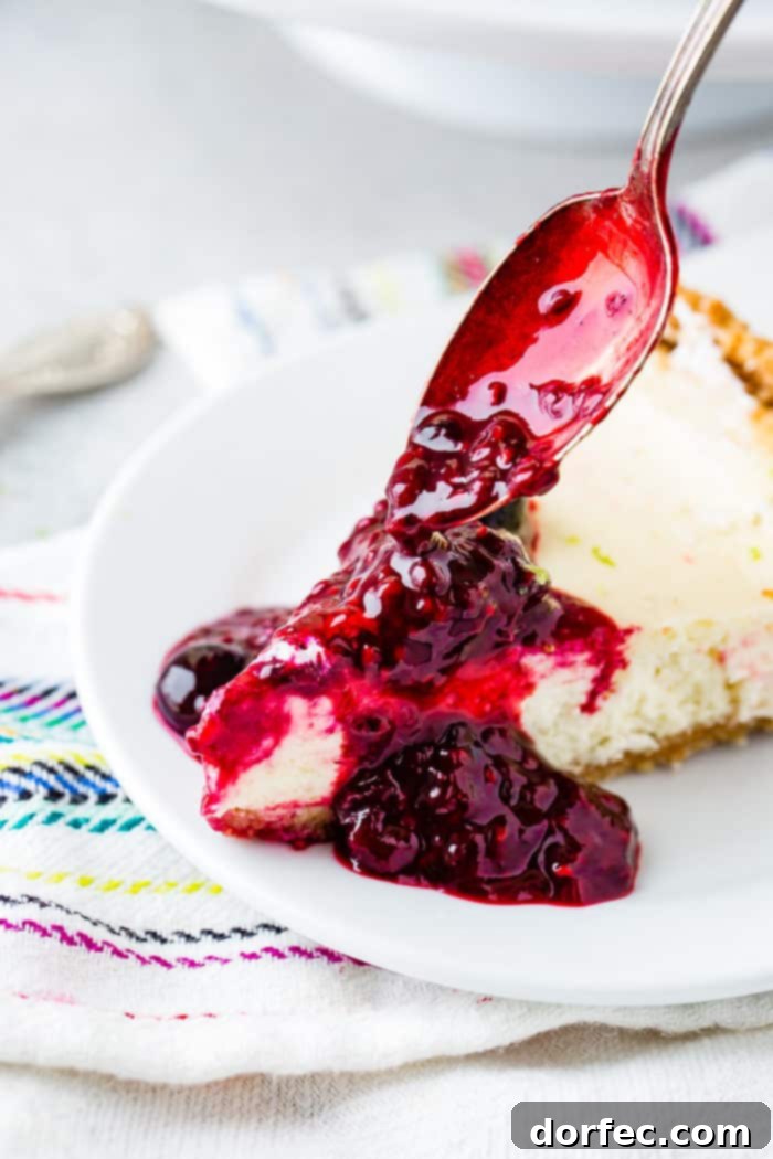 An enticing shot of a spoonful of vibrant triple berry sauce being generously poured over a slice of lime cheesecake, promising a delightful combination of flavors and textures.