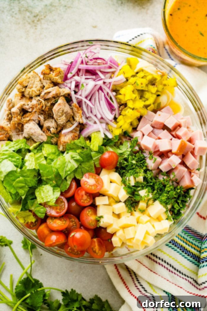 A photo of a large glass bowl full of all the ingredients for cuban pasta salad.