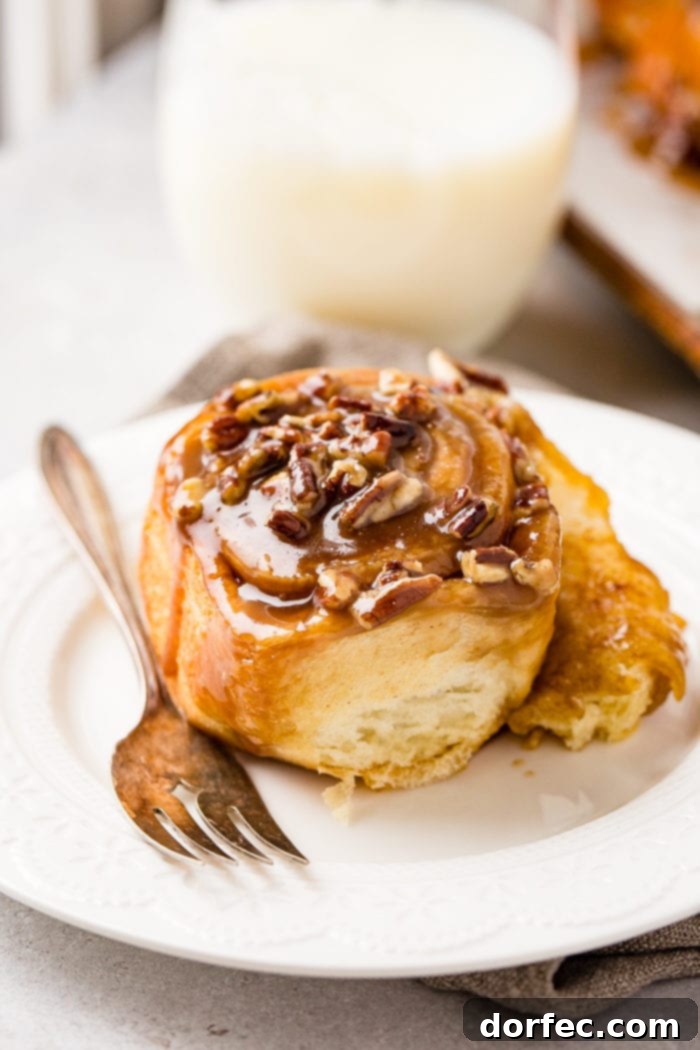 Caramel Pecan Sticky Buns 5 A photo of a sticky bun sitting on a white plate with a fork next to it.