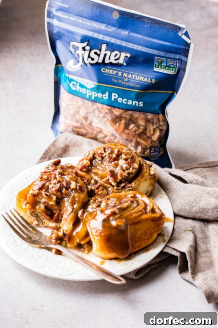 Caramel Pecan Sticky Buns 8 A photo of three sticky buns on a white plate with a fork sitting next to them and a bag of Fisher chopped pecans in the background.