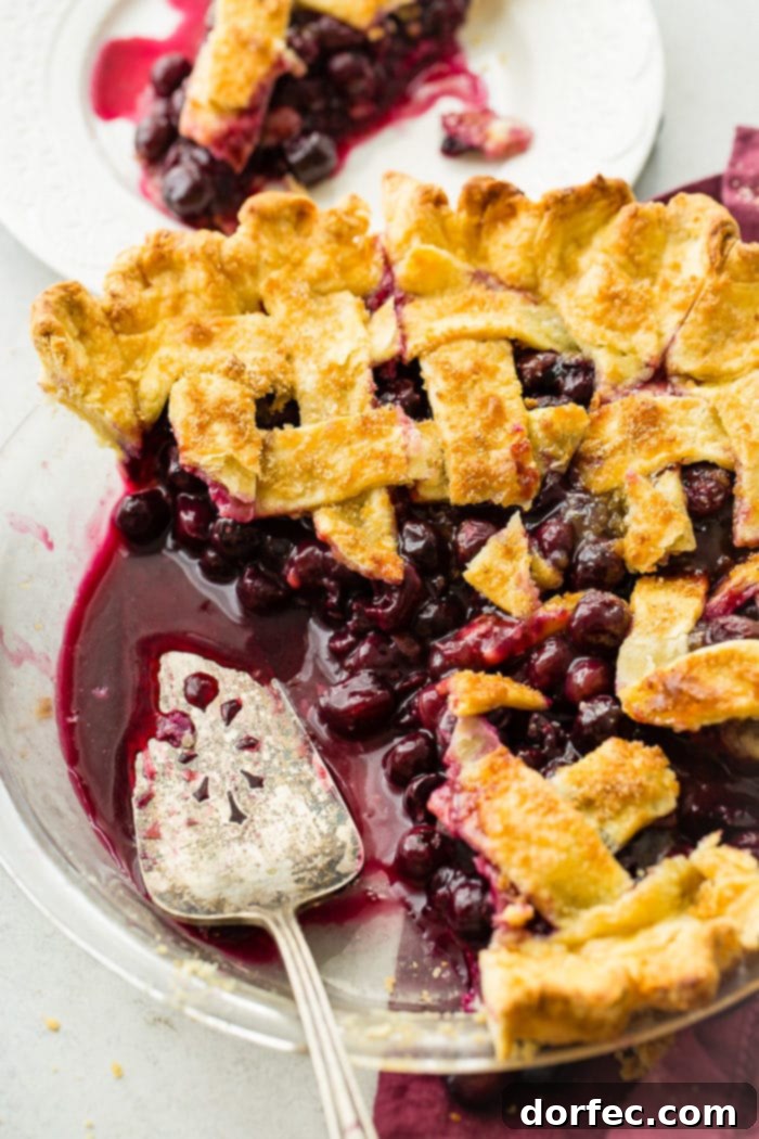 Effortless Blueberry Pie 10 A photo of a blueberry pie with a lattice top, with two slices removed and a pie server in the pan, showcasing the delicious filling.