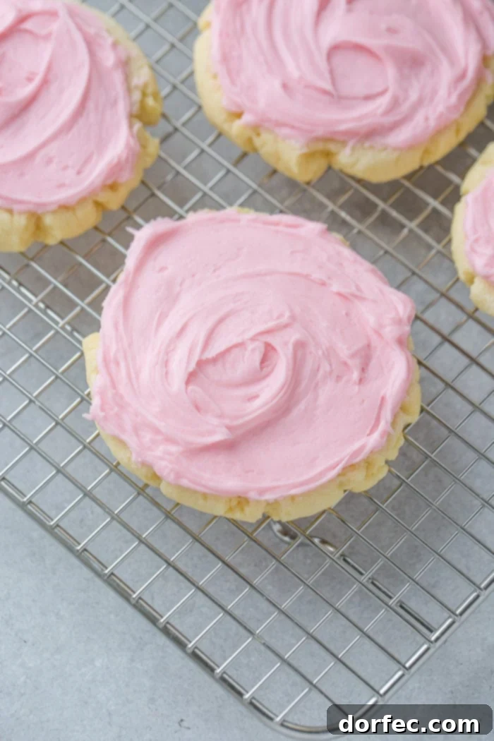 Copycat Swig Sugar Cookies and Signature Frosting 2 A photo of several soft Swig Sugar Cookies with pink frosting centered on one cookie. They are arranged on a cooling rack, highlighting their smooth texture and vibrant frosting.