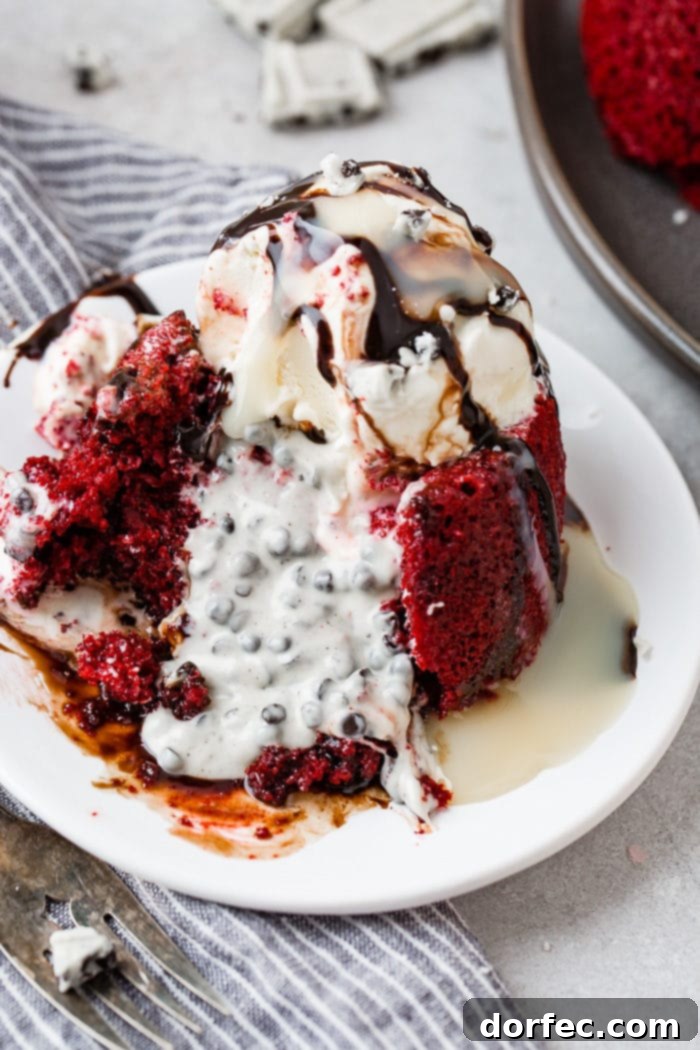 A photo of a red velvet molten lava cake filled with cookies and cream chocolate spilling out of the cake and with a scoop of vanilla ice cream on top and chocolate sauce.