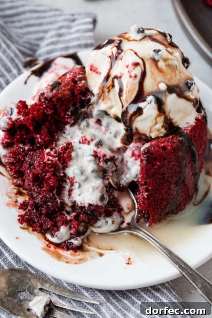 A photo of a red velvet molten lava cake with cookies and cream filling that has been cut into and spilled all over the plate. It is topped with ice cream and chocolate sauce.