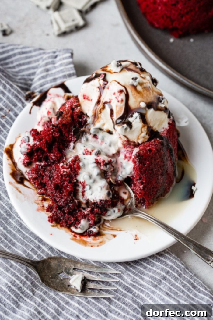 A photo of a red velvet molten lava cake with cookies and cream filling that has been cut into and spilled all over the plate. It is topped with ice cream and chocolate sauce.