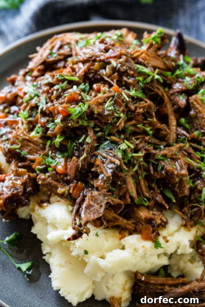 Fork-Tender Beef Roast 6 A close up photo of a pile of mashed potatoes on it covered in juicy shredded braised beef topped with chopped fresh parsley.