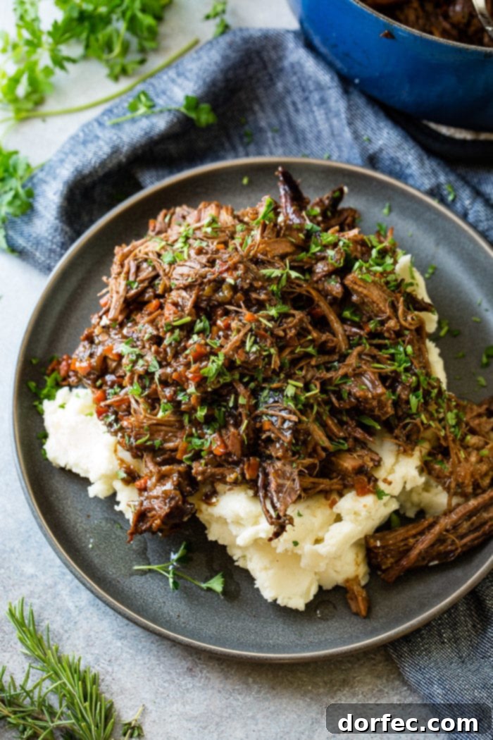 Fork-Tender Beef Roast 8 A photo of a dark gray plate with a pile of mashed potatoes on it covered in juicy shredded braised beef topped with chopped fresh parsley.