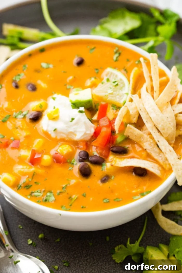 A photo of a white bowl of chicken tortilla soup topped with sour cream, a lime wedge, and tortilla strips.