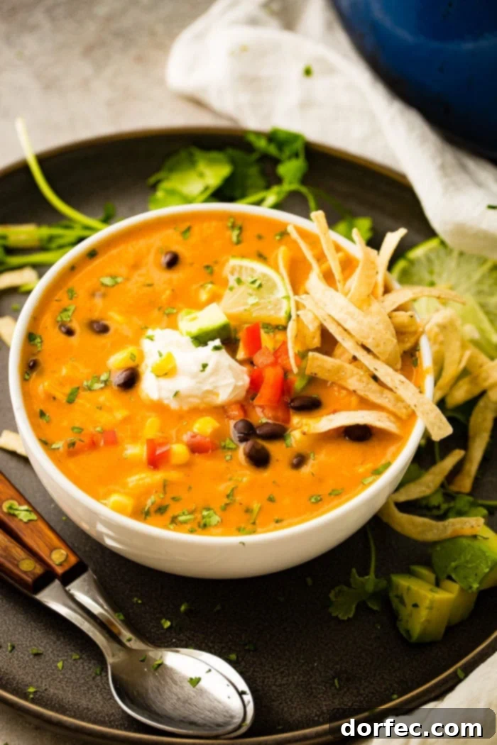 A photo of a white bowl of chicken tortilla soup topped with sour cream, a lime wedge, and tortilla strips with a spoon laying next to the bowl.