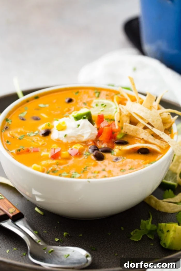 A photo of a white bowl of chicken tortilla soup topped with sour cream, a lime wedge, and tortilla strips.