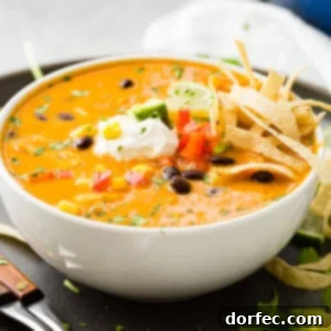 An aerial photo of a white bowl of chicken tortilla soup topped with sour cream, a lime wedge, and tortilla strips.