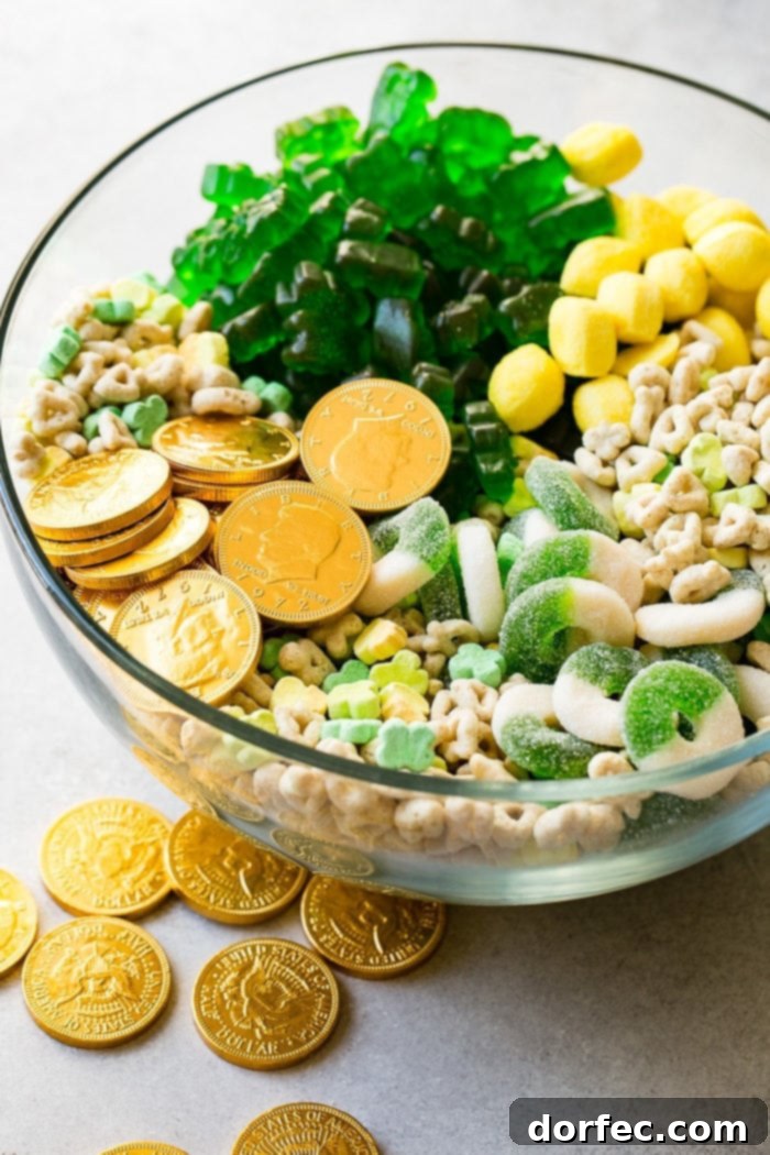 Instant Pot o' Gold Snack Mix 4 A striking image of a large, clear glass bowl filled to the brim with a lively blend of St. Patrick's Day themed candies and cereal. The photograph brilliantly showcases the vibrant green gummy candies, shimmering gold chocolate coins, and the diverse, colorful marshmallows from Lucky Charms cereal, all mixed together, inviting a celebratory indulgence.