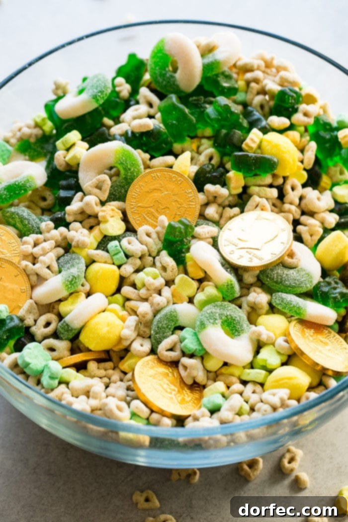 Instant Pot o' Gold Snack Mix 6 An inviting overhead view of a large, polished glass bowl, artfully arranged with a vibrant medley of St. Patrick's Day themed candies and Lucky Charms cereal. The colorful components are separate but ready to be thoroughly mixed, promising a delicious and visually appealing snack perfect for celebration.