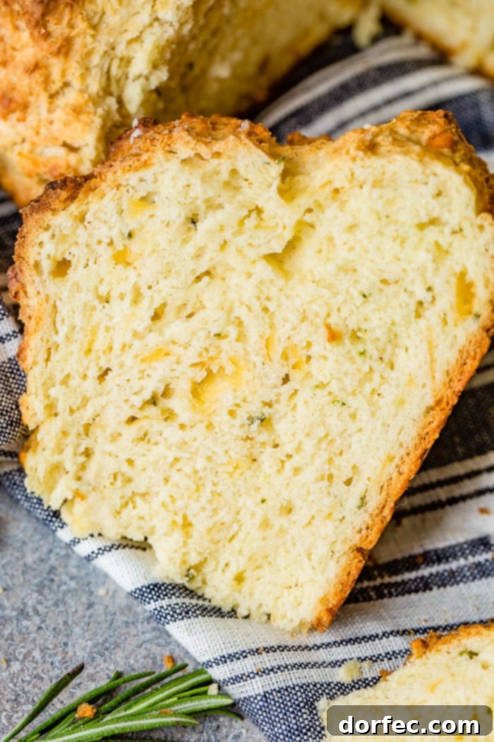 Savory Garlic Cheddar Herb Irish Soda Bread 3 A photo of a perfectly sliced piece of garlic cheddar herb irish soda bread sitting on a blue and white striped cloth napkin, showcasing its cheesy interior.