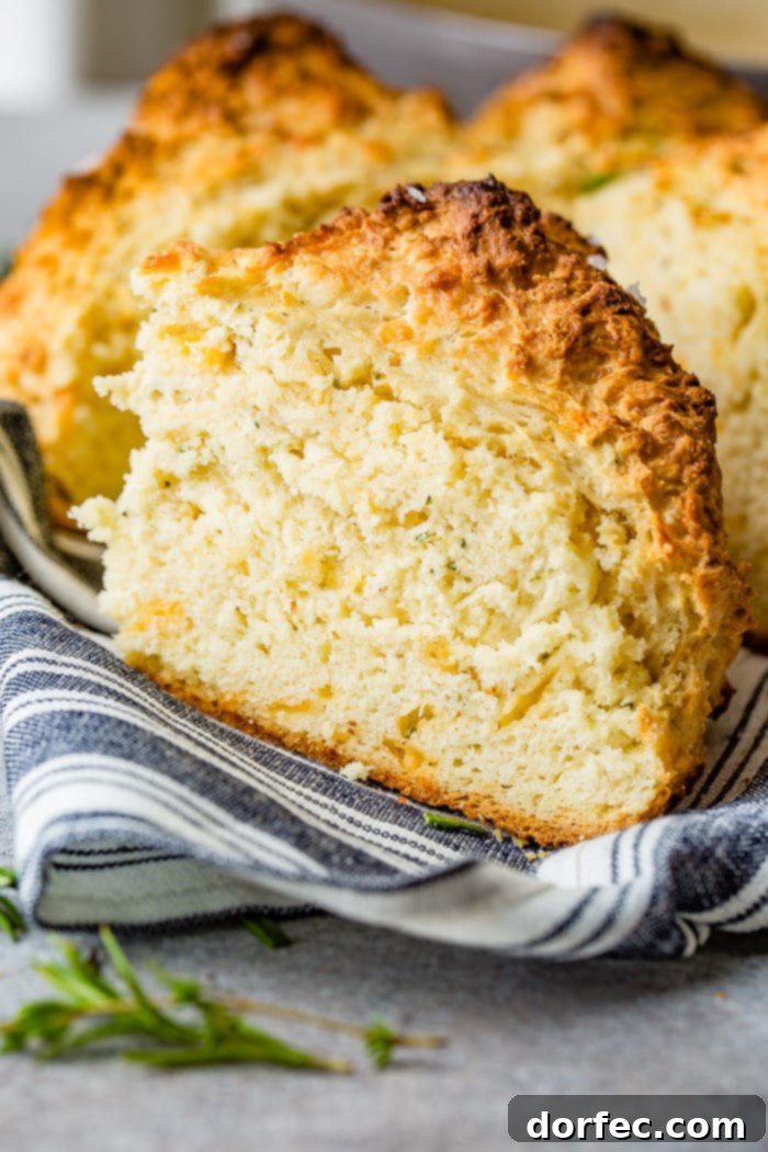 Savory Garlic Cheddar Herb Irish Soda Bread 4 A detailed photo of a slice of garlic cheddar herb irish soda bread resting on a blue and white striped cloth napkin, emphasizing its rich texture and herb flecks.