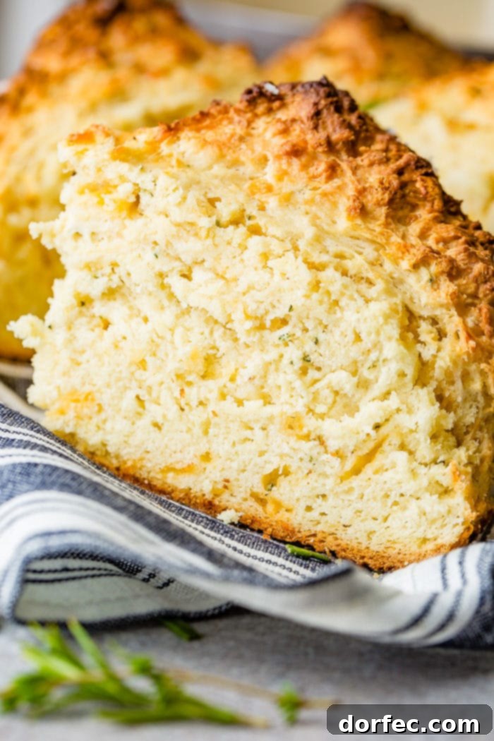 Savory Garlic Cheddar Herb Irish Soda Bread 6 A close-up photo of a generous slice of garlic cheddar herb irish soda bread on a blue and white striped cloth napkin, showcasing its abundant cheese.