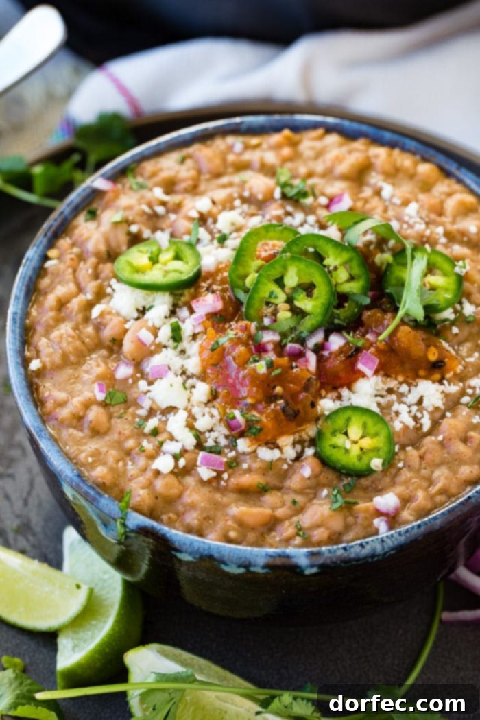 A photo of a dark blue bowl full of refried beans topped with fresh sliced jalapeno, diced purple onion, cotija cheese, and salsa.