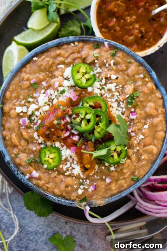A photo of a dark blue bowl full of refried beans topped with fresh sliced jalapeno, diced purple onion, cotija cheese, and salsa.