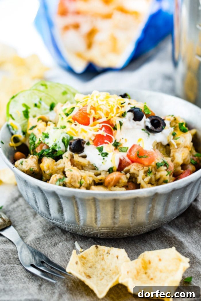 Flavor-Packed Instant Pot Cilantro Lime Chicken Burrito Bowls 17 A top-down view of a silver bowl filled with cilantro lime chicken and rice, accompanied by pinto beans, and beautifully adorned with sour cream, sliced black olives, grated Colby Jack cheese, fresh cilantro, and lime wedges.
