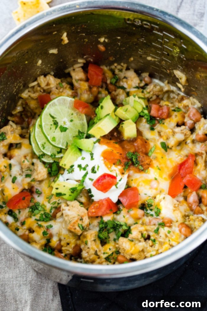 Flavor-Packed Instant Pot Cilantro Lime Chicken Burrito Bowls 18 The Instant Pot filled with cilantro lime chicken and rice, topped with melted Colby Jack cheese, diced tomatoes, a generous dollop of sour cream, creamy avocado chunks, and fresh cilantro, with lime slices on the side.
