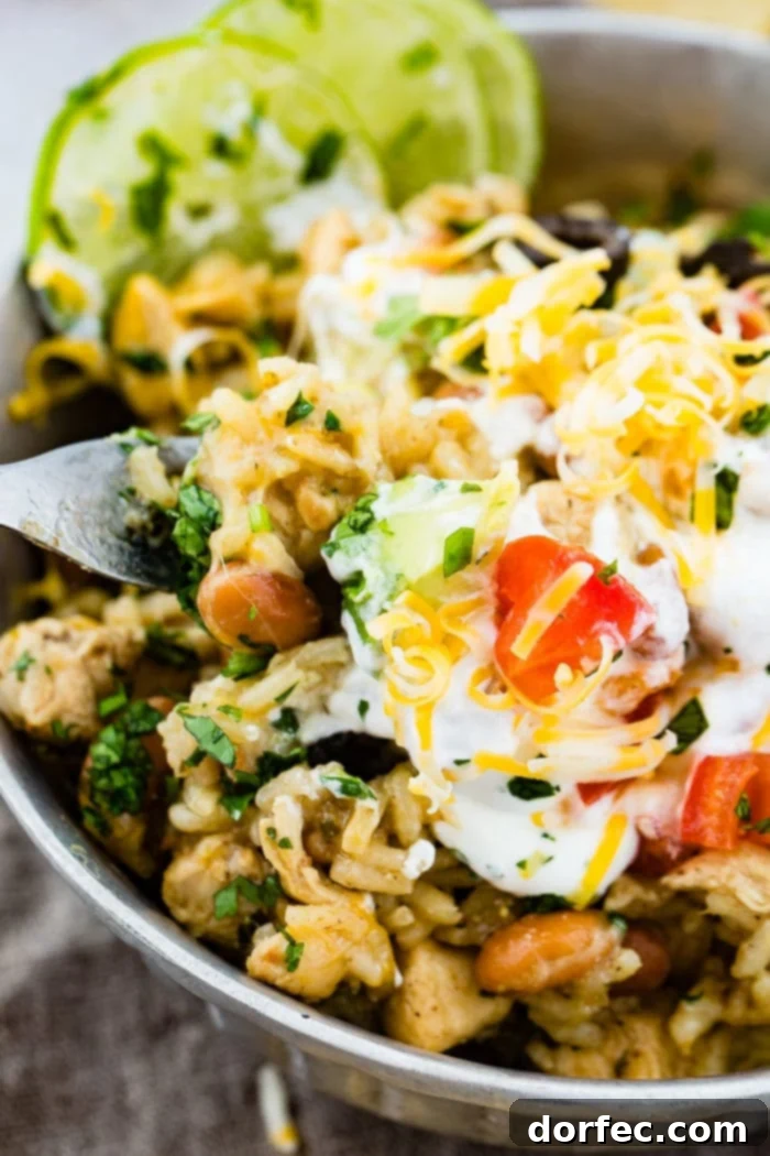 Flavor-Packed Instant Pot Cilantro Lime Chicken Burrito Bowls 19 A close-up shot of a silver bowl showcasing the texture and vibrant colors of the cilantro lime chicken and rice with pinto beans, artfully topped with sour cream, sliced olives, grated Colby Jack cheese, fresh cilantro, and lime.