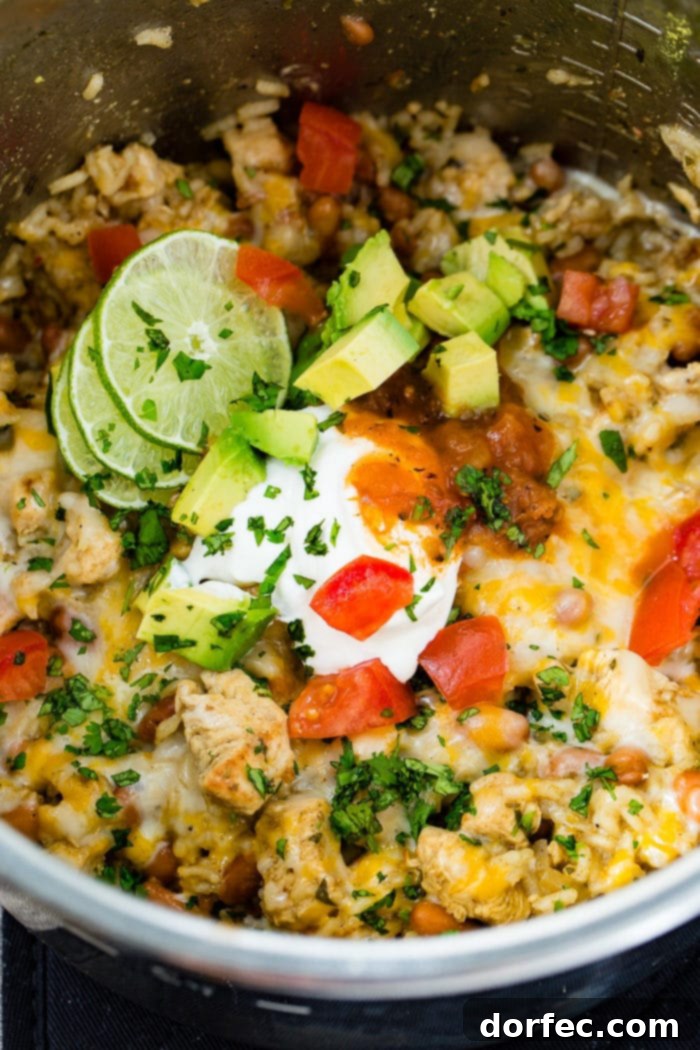 Flavor-Packed Instant Pot Cilantro Lime Chicken Burrito Bowls 20 A tantalizing view of the cilantro lime chicken and rice, along with pinto beans, directly in the Instant Pot, covered with melted Colby Jack cheese and garnished with fresh diced tomatoes, sour cream, avocado, cilantro, and lime.