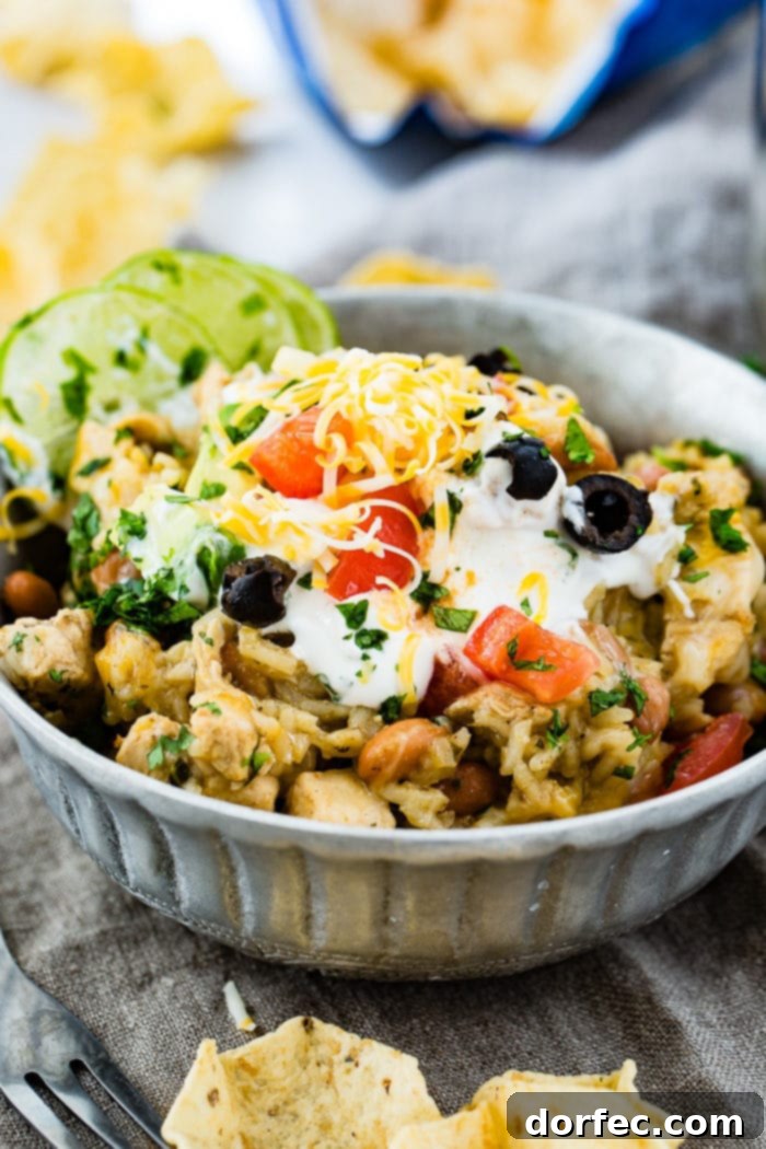 Flavor-Packed Instant Pot Cilantro Lime Chicken Burrito Bowls 21 A beautifully composed silver bowl featuring Instant Pot cilantro lime chicken and rice with pinto beans, elegantly topped with sour cream, sliced olives, grated Colby Jack cheese, chopped fresh cilantro, and lime wedges.