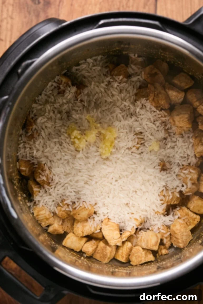 Flavor-Packed Instant Pot Cilantro Lime Chicken Burrito Bowls 6 Uncooked rice and minced garlic being stirred into the Instant Pot with seared chicken.