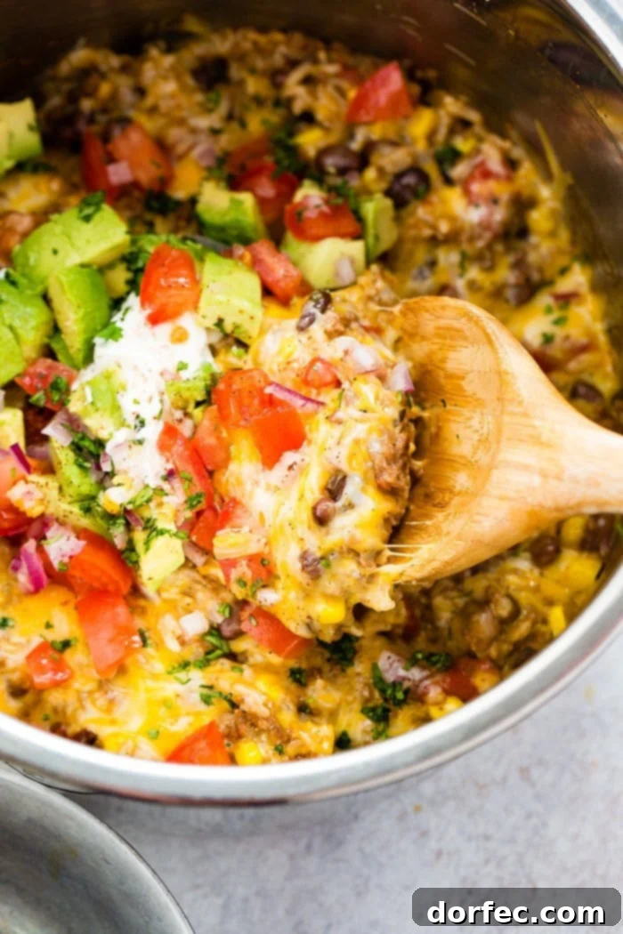 A tantalizing Instant Pot ground beef burrito bowl with a scoop taken out, revealing layers of seasoned beef, rice, and beans, garnished with fresh toppings.