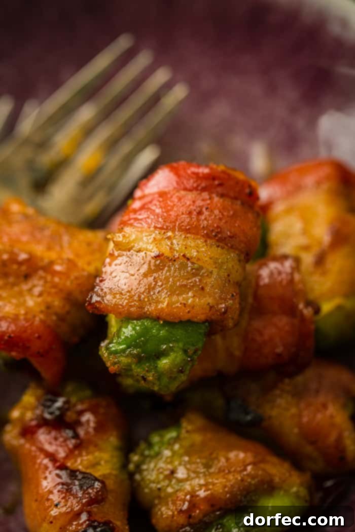 Crispy Bacon Avocado Wraps 2 A dark purple plate with a few forks on the left, and a pile of avocado pieces with brown sugar bacon wrapped around them which have been baked and are crispy!