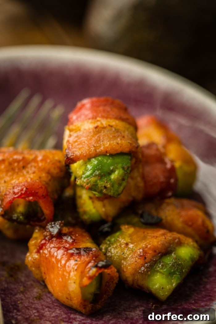 Crispy Bacon Avocado Wraps 5 Bacon wrapped around pieces of green avocados with brown sugar and baked until crispy, all piled up on a plate as an easy appetizer recipe