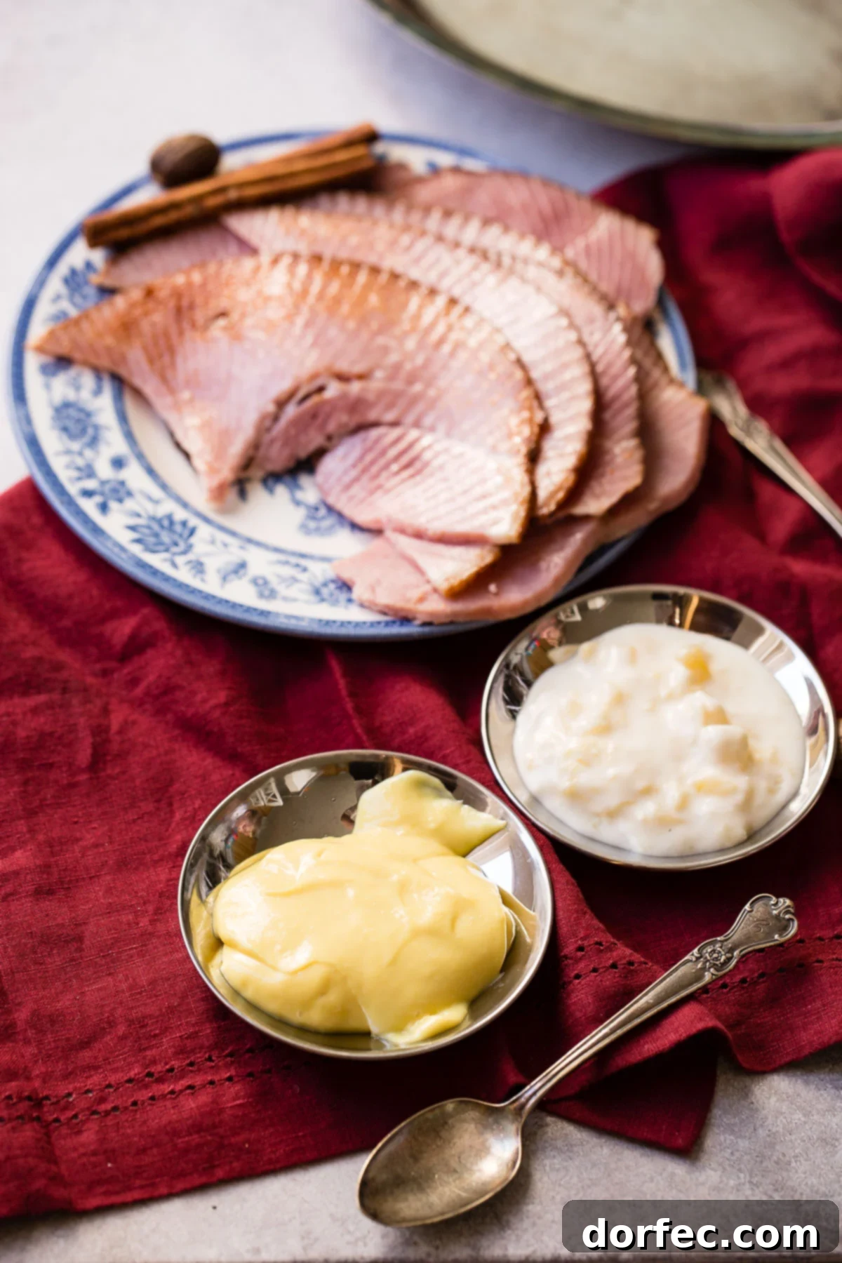 a platter of ham slices in the background with two small bowls of dipping sauces sitting next to the platter