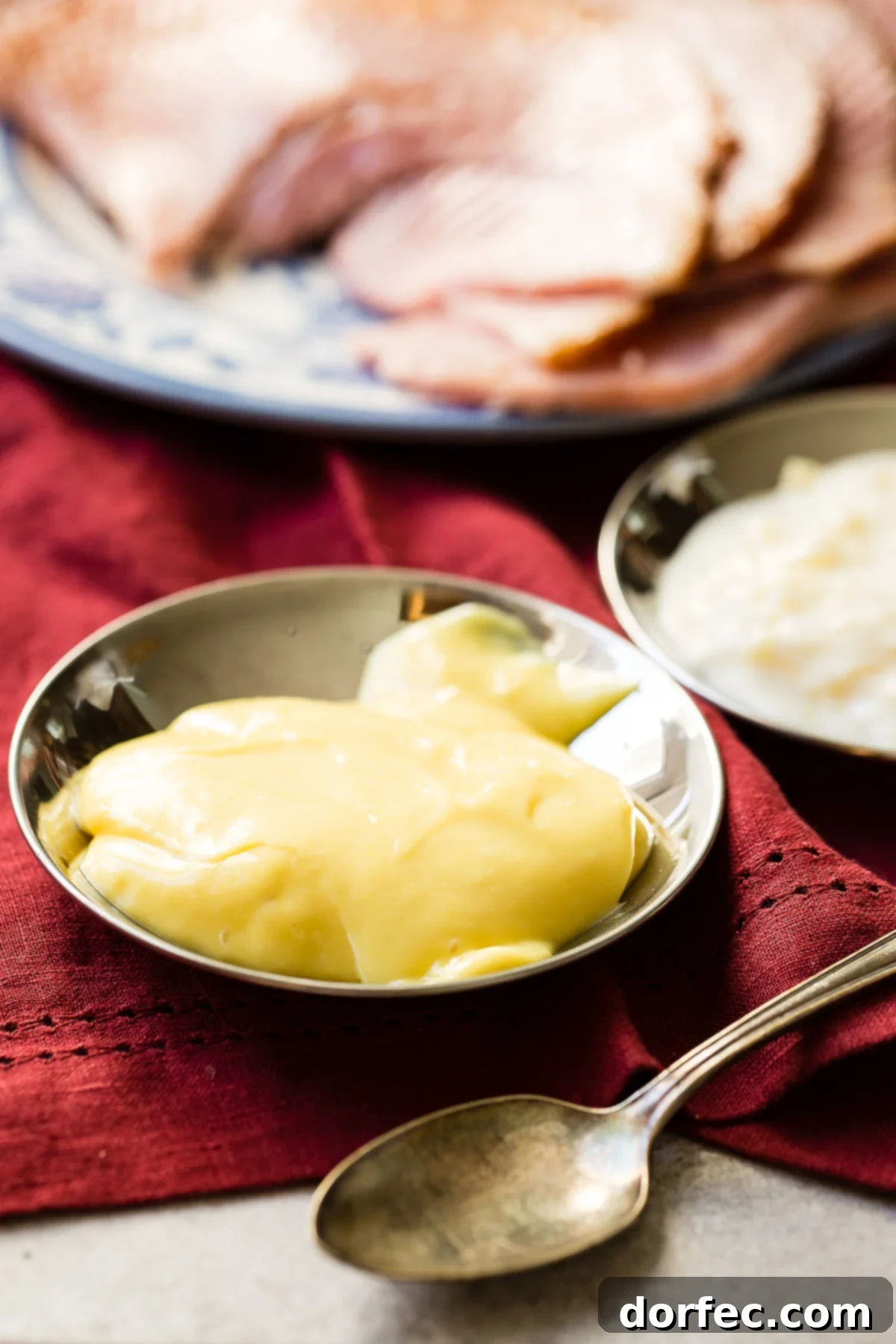 a photo of a small dish full of honey mustard dipping sauce for ham with a platter of ham slices behind it